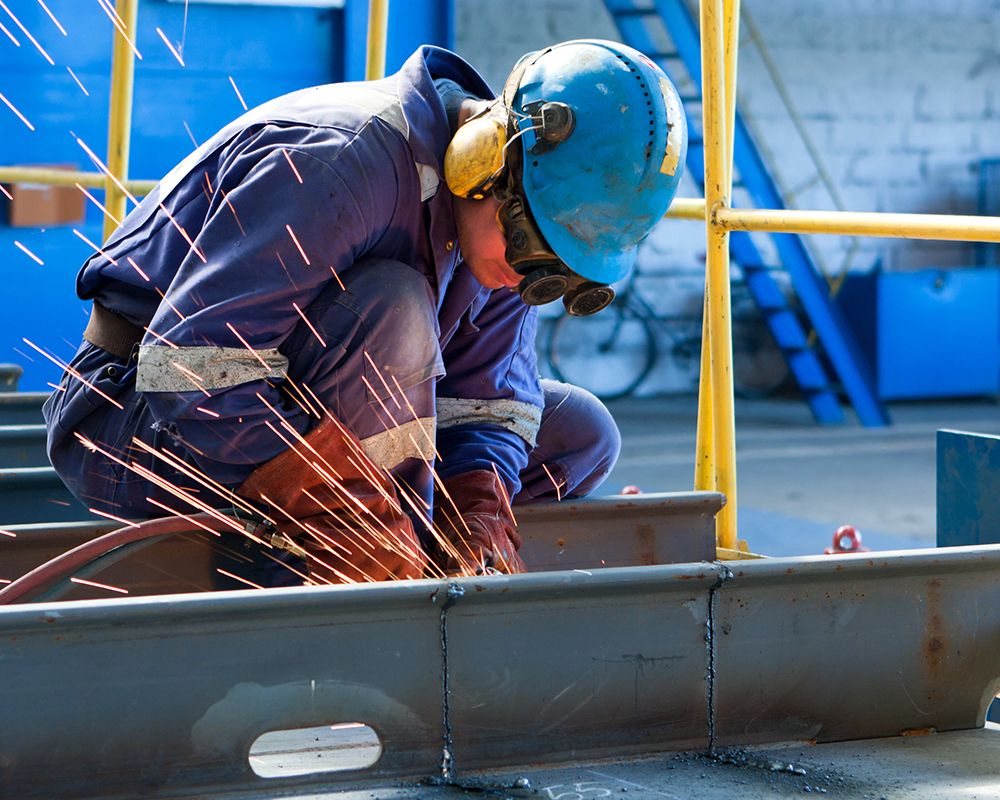 Arbeiter mit Schutzkleidung und Helm beim Schweißen einer Stahlkonstruktion